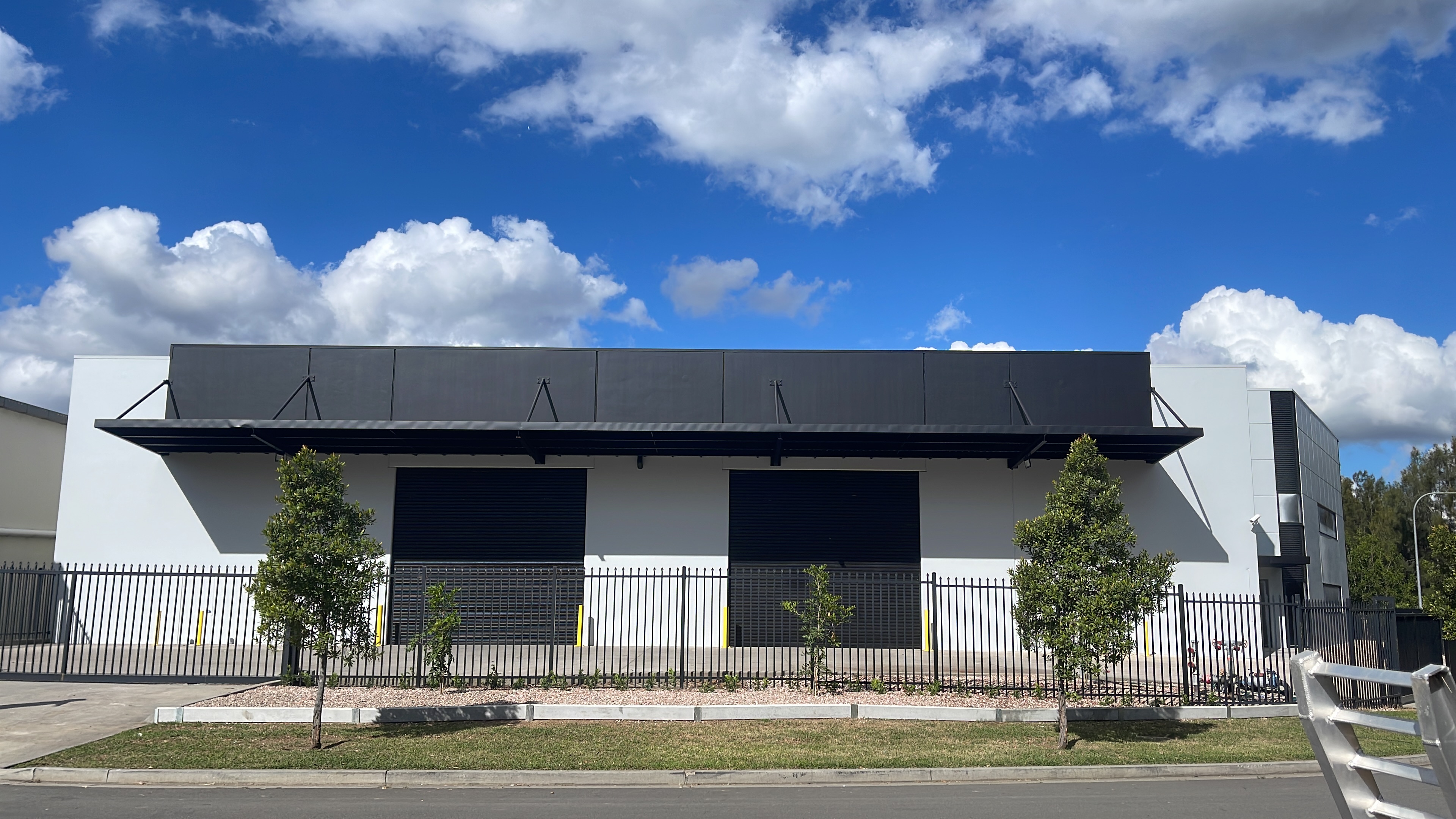 Warehouse with black painted steel canopy, black roller doors and new trees